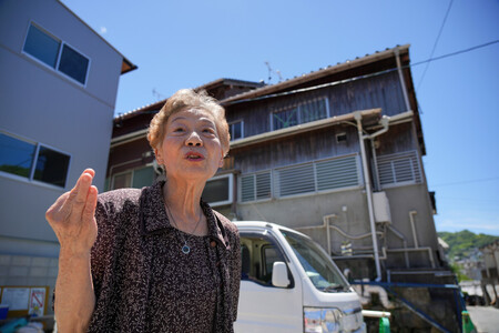 被爆当時に住んでいた自宅(右奥)の前で、2階から見た原爆投下の瞬間について語る八木道子さん=7月29日、長崎市