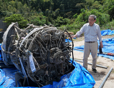 引き揚げられた紫電改と、NPO法人「北薩の戦争遺産を後世に遺す会」代表の肥本英輔さん=9日、鹿児島県出水市