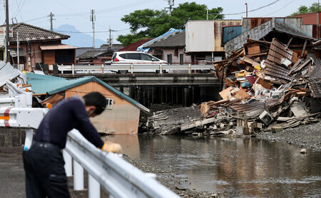 熊本県八代市を流れる鏡川沿いで倒壊したままの建物=10日午前