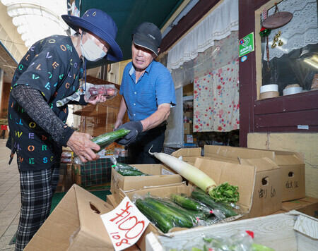中心市街地の本町アーケード街の青果店「やさい村」で野菜を販売する店主の谷次雄さん(右)=27日午前、熊本県八代市